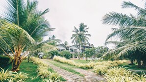 A pathway leading to a building surrounded by palm trees and well-maintained greenery. - Samudra Beach Resort (Rekawa)