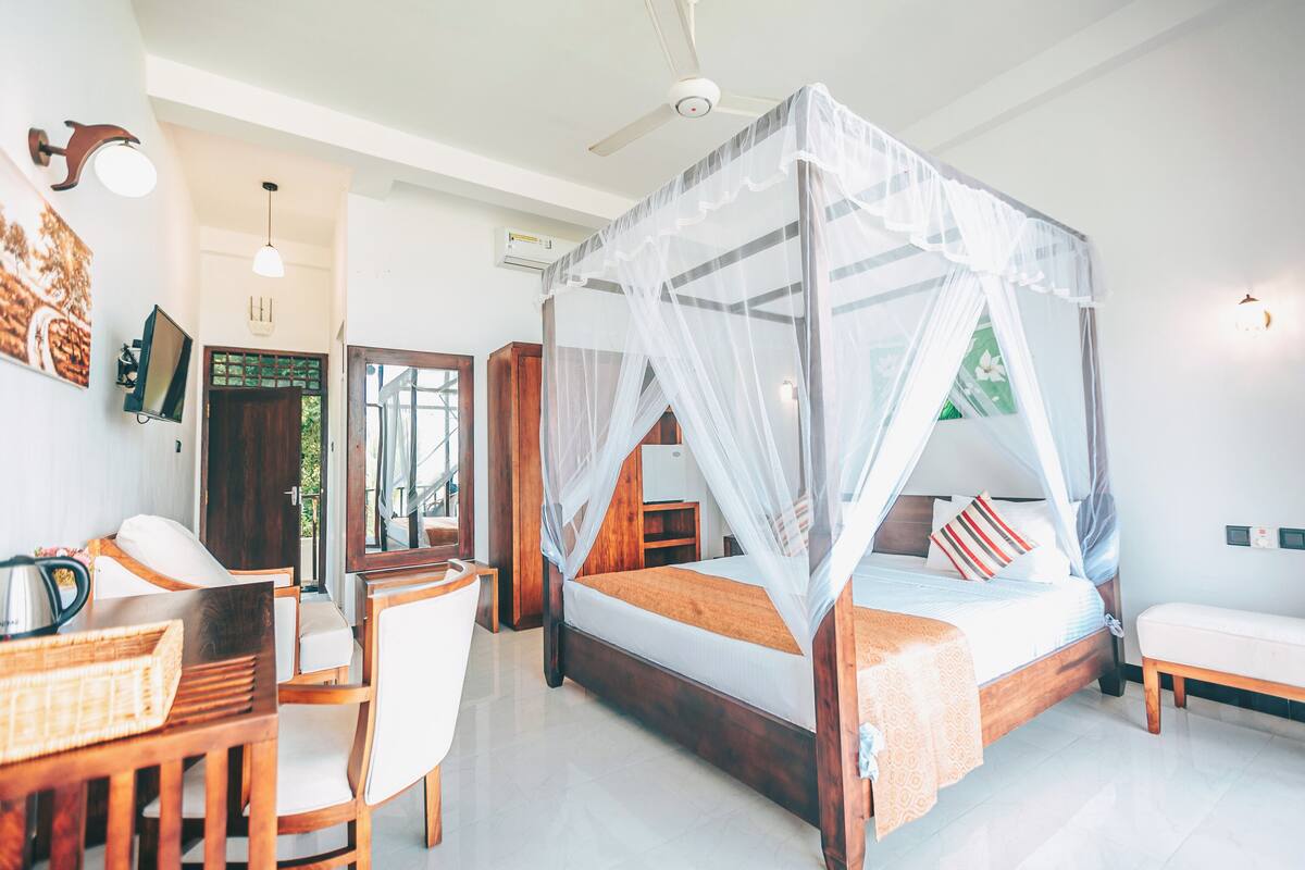 A bedroom with a four-poster bed, a desk with a chair, and a bedside table.
