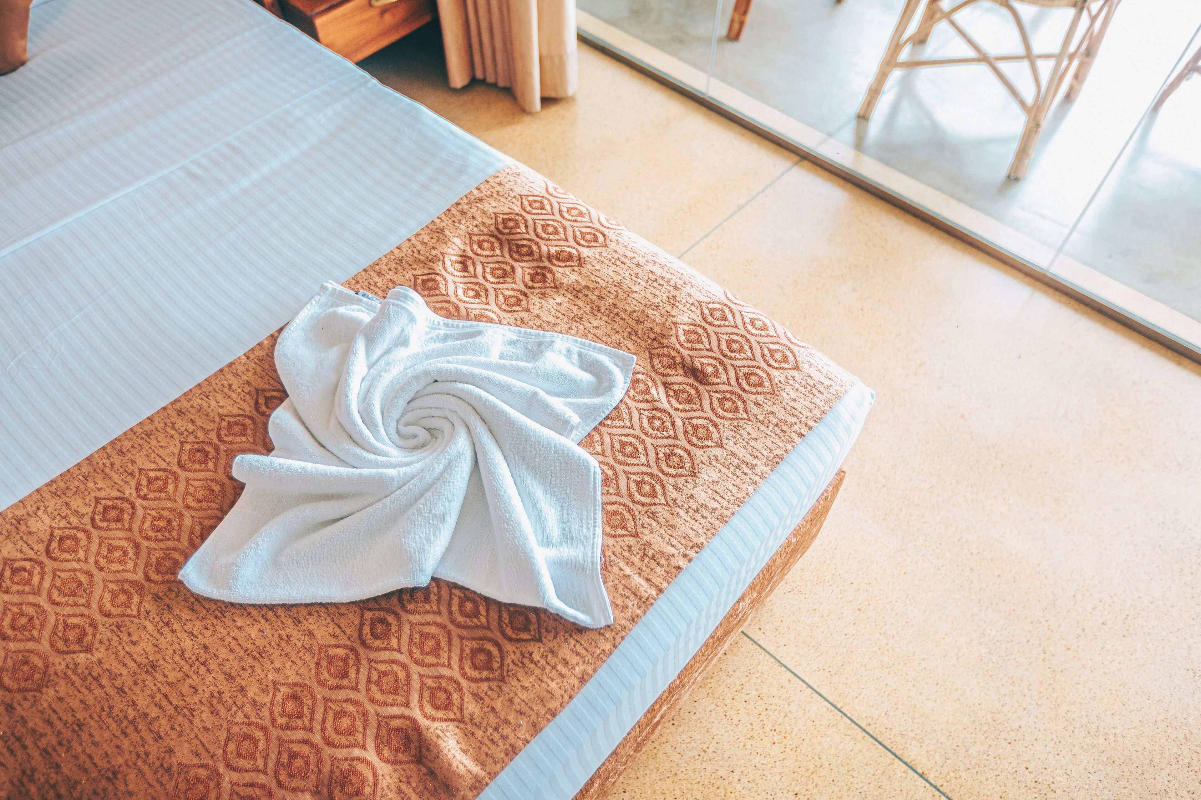 A neatly made bed with a patterned brown bedspread and a folded white towel.