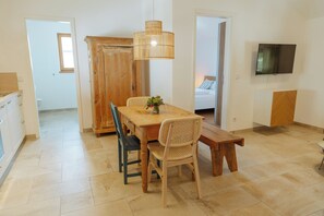A dining area with a wooden table, two chairs, a bench, a wicker chair, and a hanging light fixture.