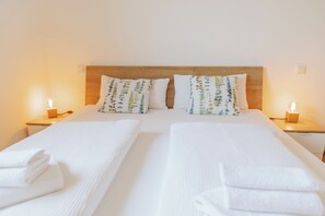 A double bed with white linens, two pillows with a leaf pattern, and bedside lamps.