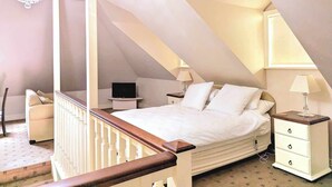 A bedroom with a sloped ceiling, a bed, bedside tables, a chandelier, and a staircase. - Tanwarra Lodge (Sofala)