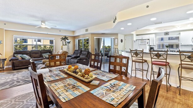 A spacious living room with a dining area, a kitchen, and a view of the outdoors. - Oceanwalk 3BR | Sunset Estuary Views, 2 Private Balconies & Beach Walk (New Smyrna Beach)