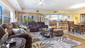A spacious living room with a brown leather sofa, a glass coffee table, and a patterned rug. - Oceanwalk 3BR | Sunset Estuary Views, 2 Private Balconies & Beach Walk (New Smyrna Beach)