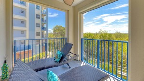 A balcony with two lounge chairs, a ceiling fan, and a view of a building and trees. - Oceanwalk 3BR | Sunset Estuary Views, 2 Private Balconies & Beach Walk (New Smyrna Beach)