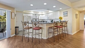 A spacious kitchen with white cabinets, a central island with bar stools, and a ceiling-mounted fish sculpture. - Oceanwalk 3BR | Sunset Estuary Views, 2 Private Balconies & Beach Walk (New Smyrna Beach)