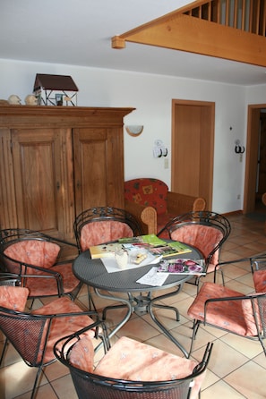 Un coin repas avec une table ronde entourée de six chaises dotées de coussins à motifs floraux, un buffet en bois et un canapé rouge à motifs.