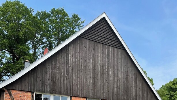 Een gebouw met twee verdiepingen, een schuin dak, een geelbruine gevel en een balkon met buitenmeubels.