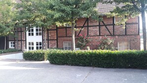 A building with a brick facade, white-framed windows, and a hedge in front. - Ferienwohnungen Landhaus Am Esch, Appartement im Erdgeschoss (Warendorf)