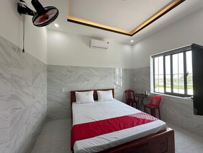 A hotel room with a bed, a red chair, a table, and a window with bars. - Phat Tai Hotel 2 (Da Nang)