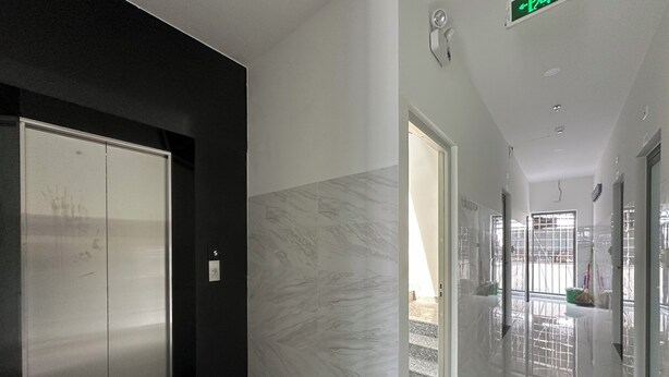 Un pasillo moderno con piso de mármol, un ascensor negro y una puerta de cristal que da a un balcón.