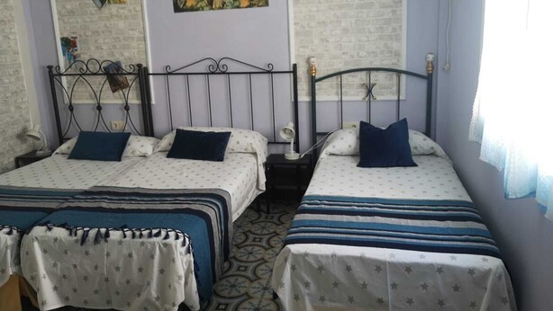 A bedroom with two beds, each with a star-patterned bedspread, a nightstand with a lamp, and wall art depicting religious figures and a cityscape.