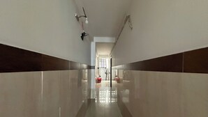 A long, narrow hallway with glossy tiled walls and a reflective floor, leading to a bright room with a window.