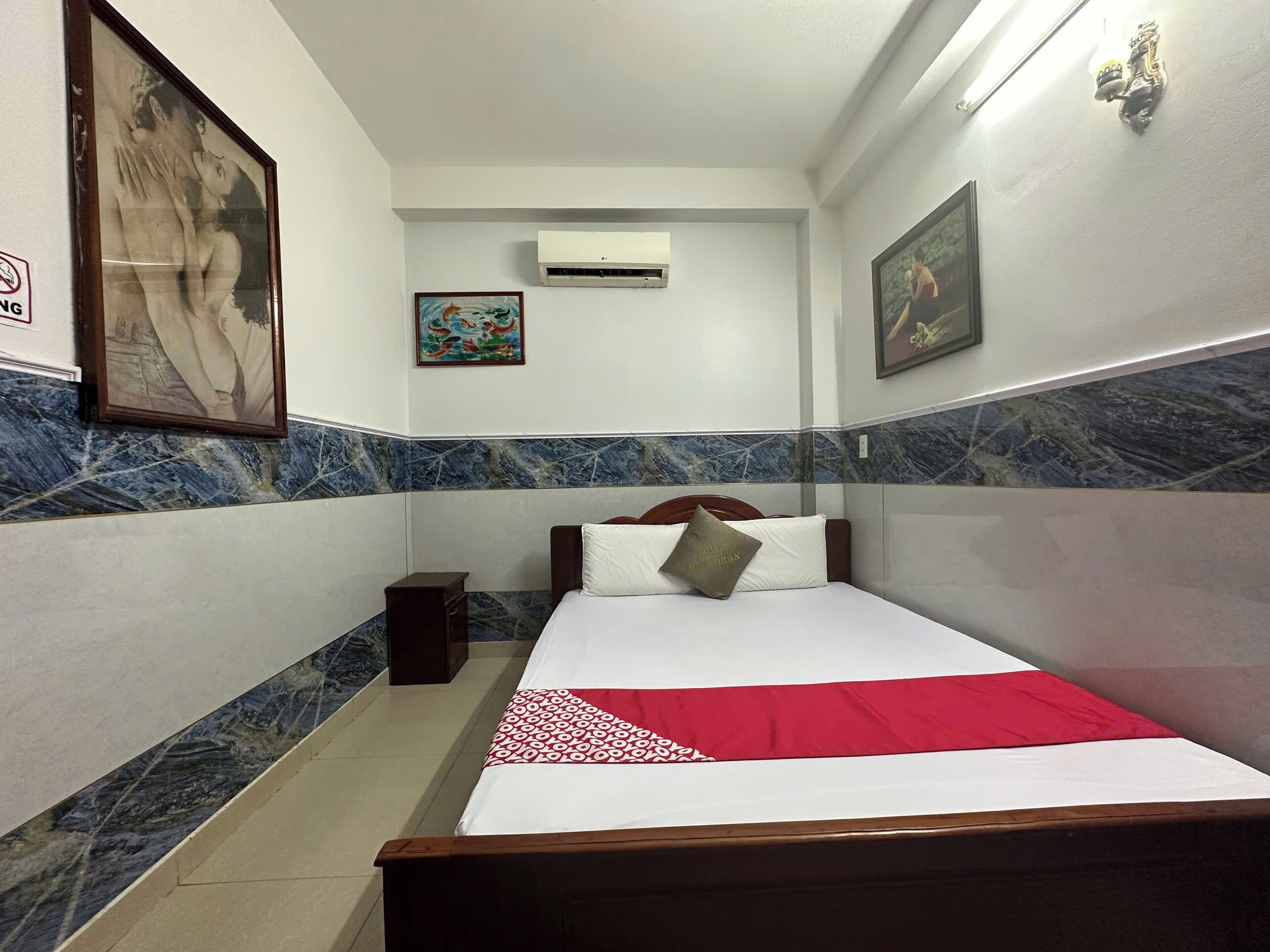 Habitación de hotel con cama, mesita de noche, aire acondicionado de pared y cuadros enmarcados.