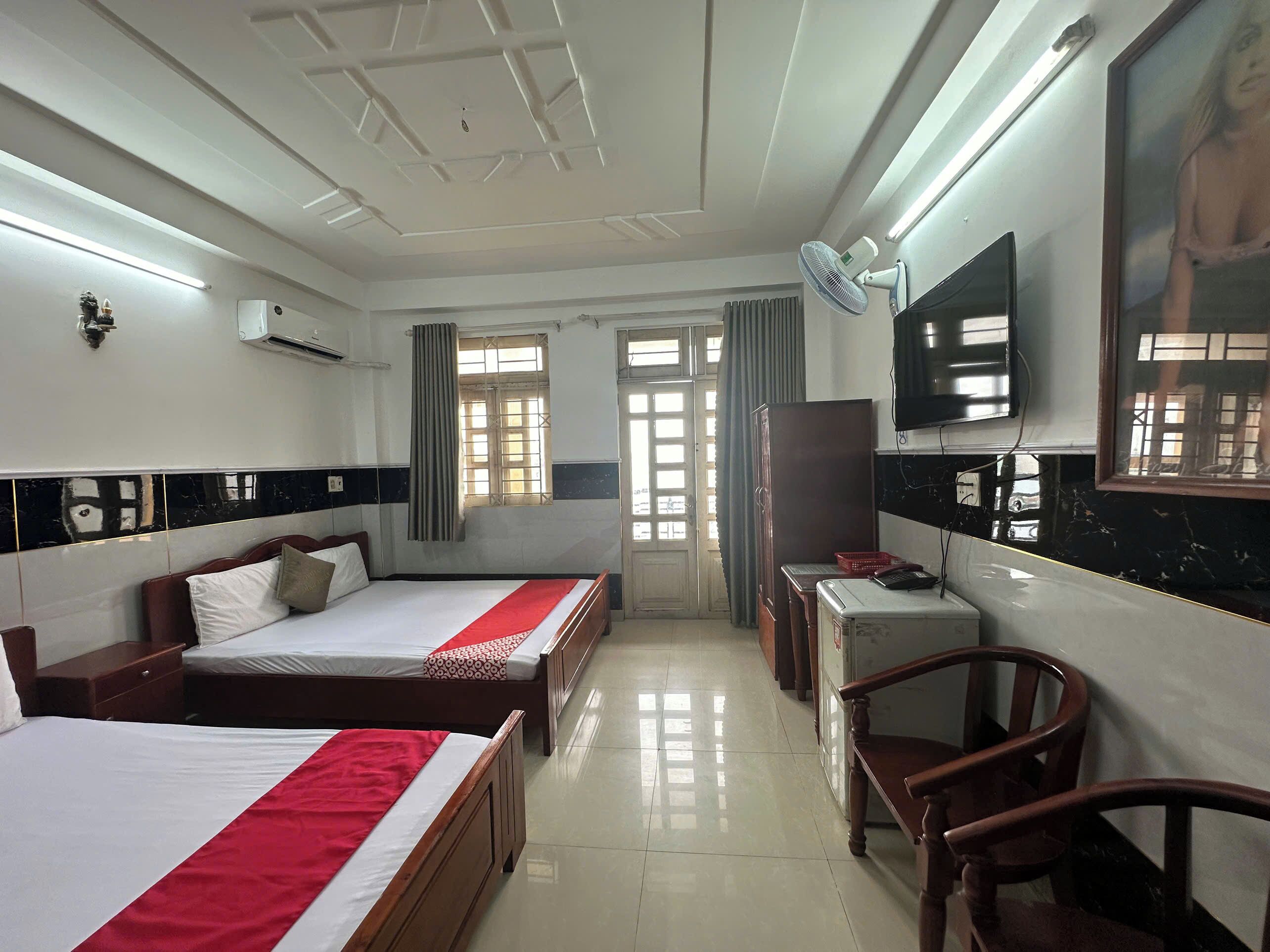 A hotel room with two beds, a desk, a chair, a TV, and a window with curtains.