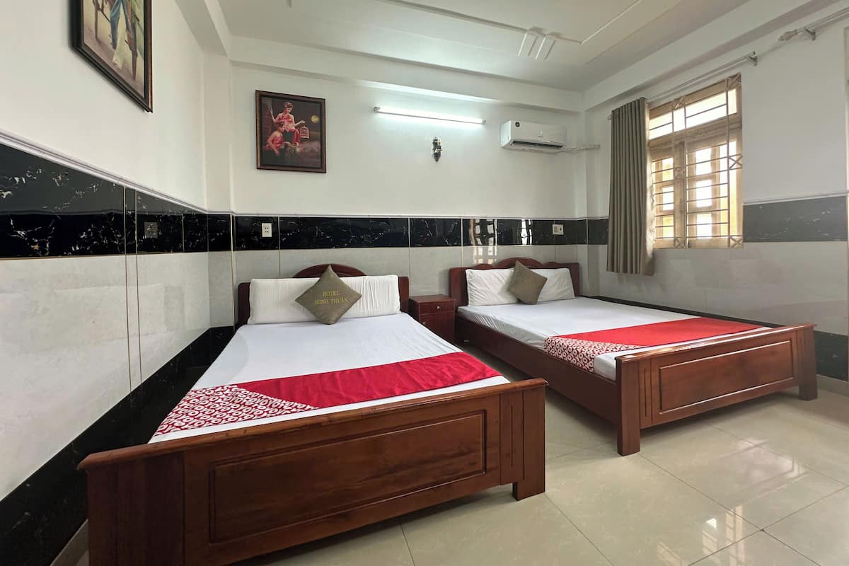 A hotel room with two wooden beds, a ceiling fan, a window with curtains, and a wall-mounted air conditioner.
