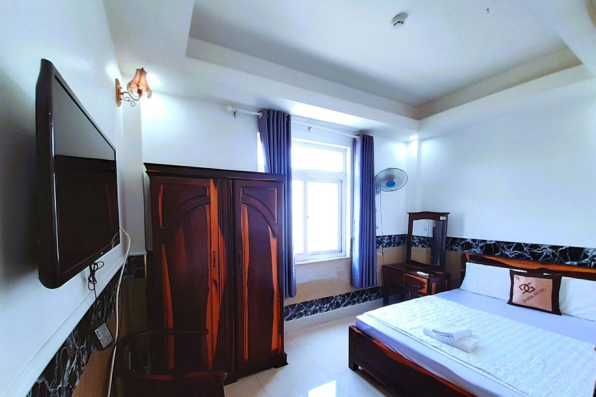 A hotel room with a bed, a TV, a wardrobe, a mirror, and a window with curtains.