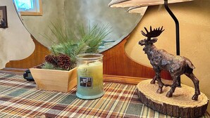En lampe, et stearinlys, en grankogle og en elgstøtte på et bord.