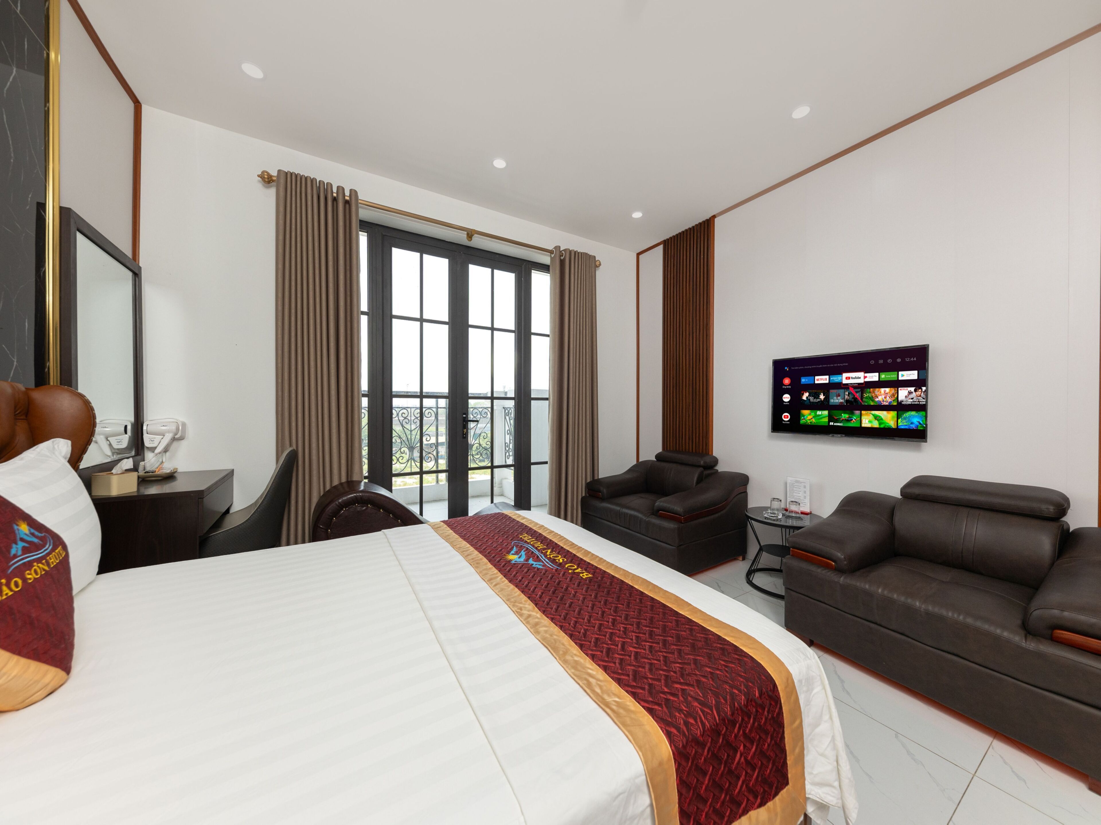 Ein Hotelzimmer mit einem großen Bett, einer Couch, einem Fernseher und einem Balkon mit Vorhängen.