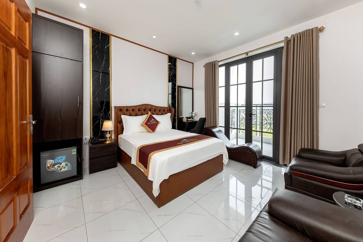 A hotel room with a large bed, a seating area, and a view of the outdoors.