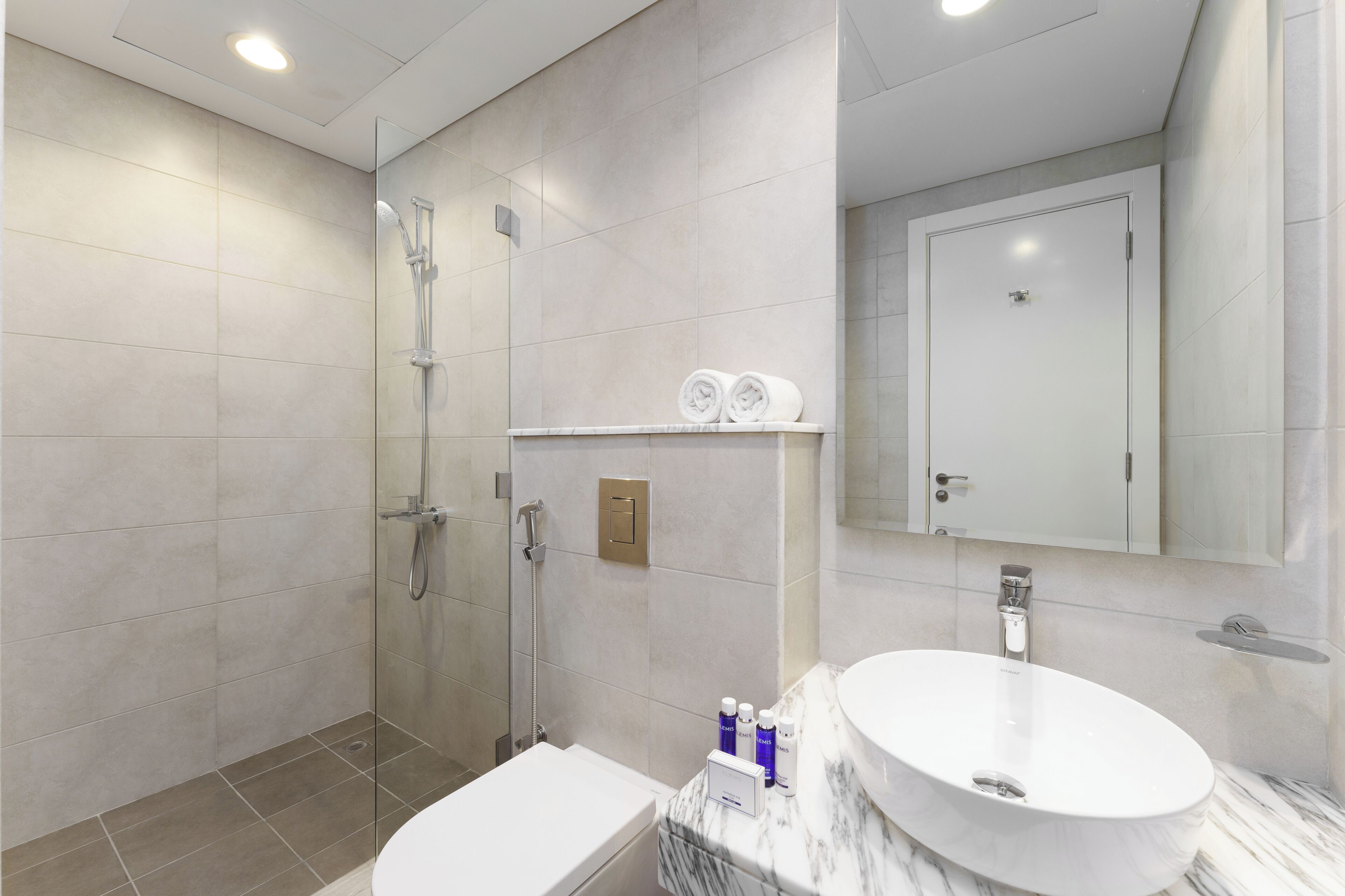 Een moderne badkamer met een douchecabine van glas, een wit wastafeltje en een marmeren aanrechtblad.