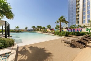A pool area with lounge chairs, palm trees, and a building with 'DURAN' signage.