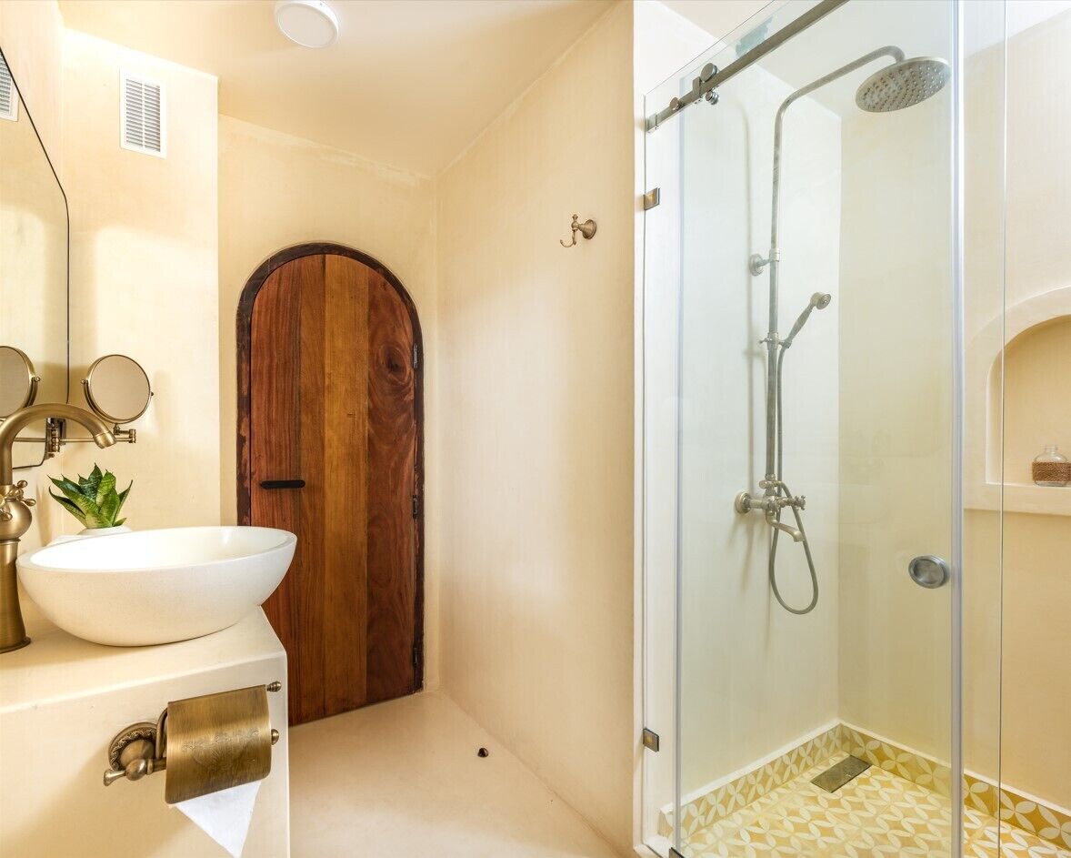 A bathroom with a wooden door, a white sink with a mirror, and a glass-enclosed shower area.