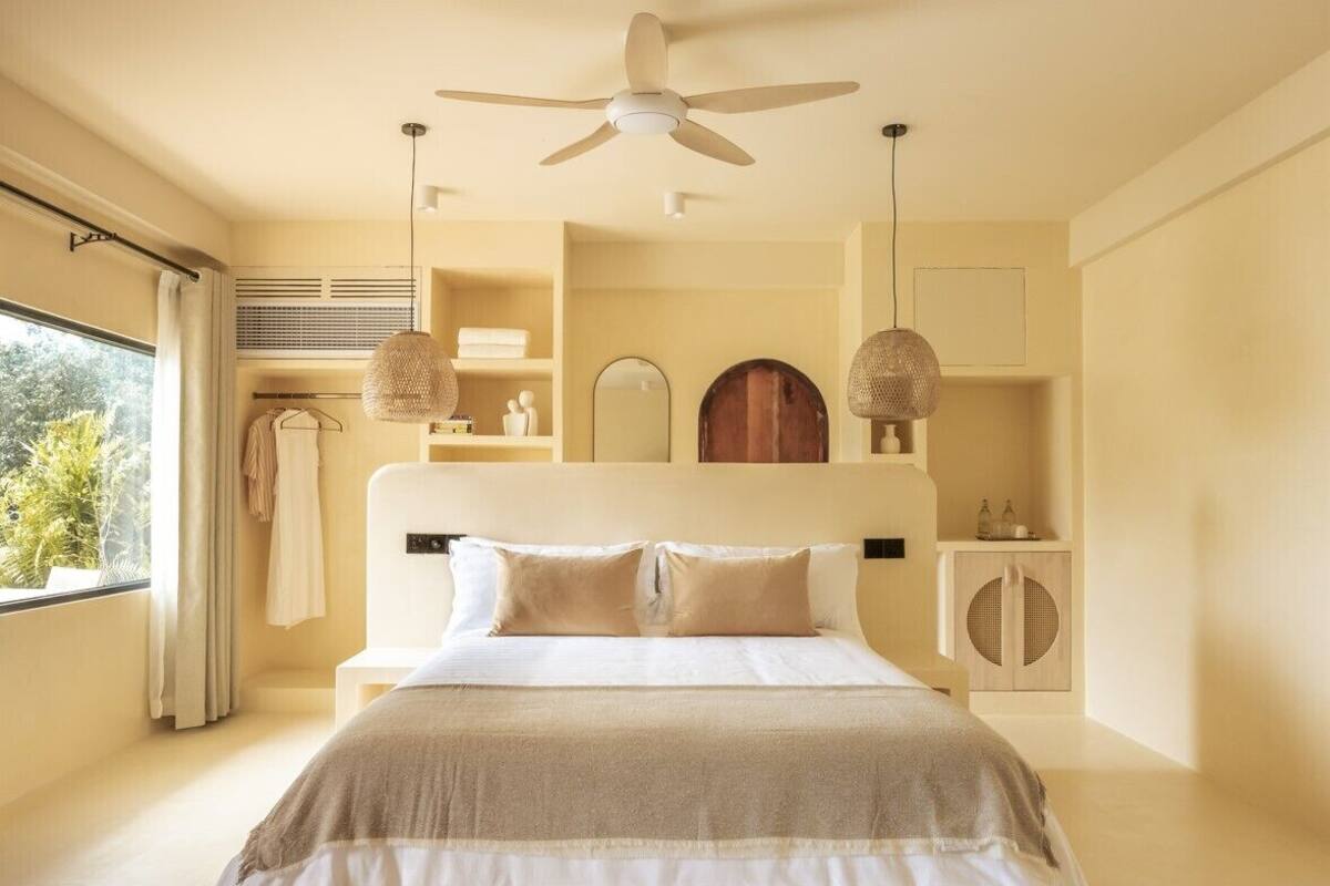 Une chambre à coucher avec un lit, un ventilateur de plafond, une fenêtre et une armoire.