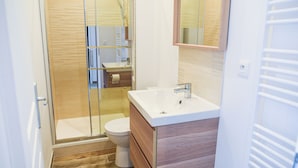 A modern bathroom with a glass shower enclosure, a white toilet, and a wooden vanity with a mirror above the sink. - Amazonia Rouen Centre by Myfrenchpat (Rouen)