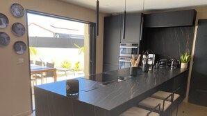 A modern kitchen with a large island, bar stools, a built-in oven, and a coffee maker. - Maison / Piscine, Proche Plages (Vic-la-Gardiole)