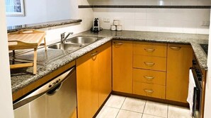Une cuisine avec des meubles en bois, un plan de travail en granit, un lave-vaisselle encastré et un dosseret carrelé.