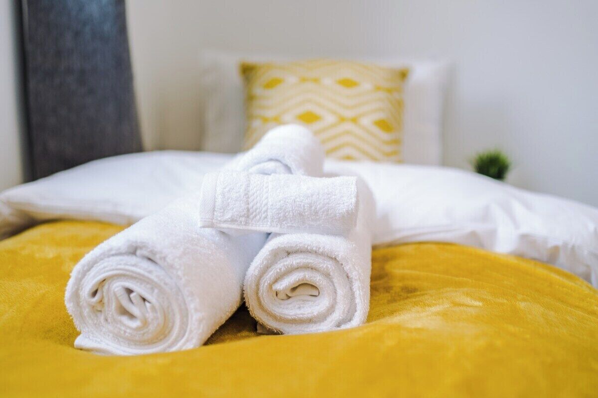 A bed with two rolled white towels and a yellow pillow.