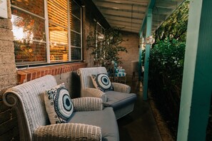 Un espace extérieur accueillant, aménagé avec des meubles en osier et des coussins, un mur en briques et une vue sur un jardin.