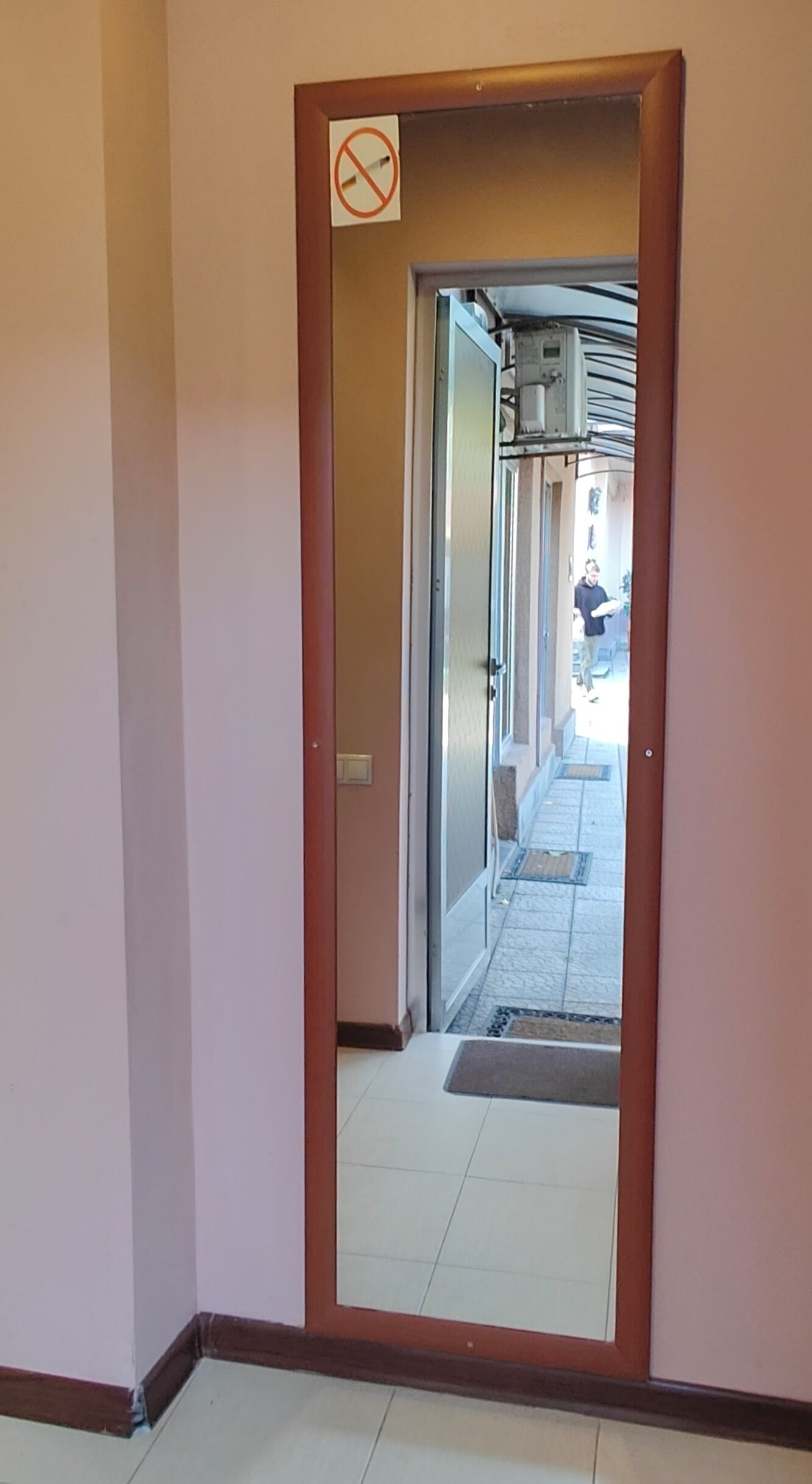 A hallway with a no-smoking sign, a door leading to an outdoor area, and a tiled floor.