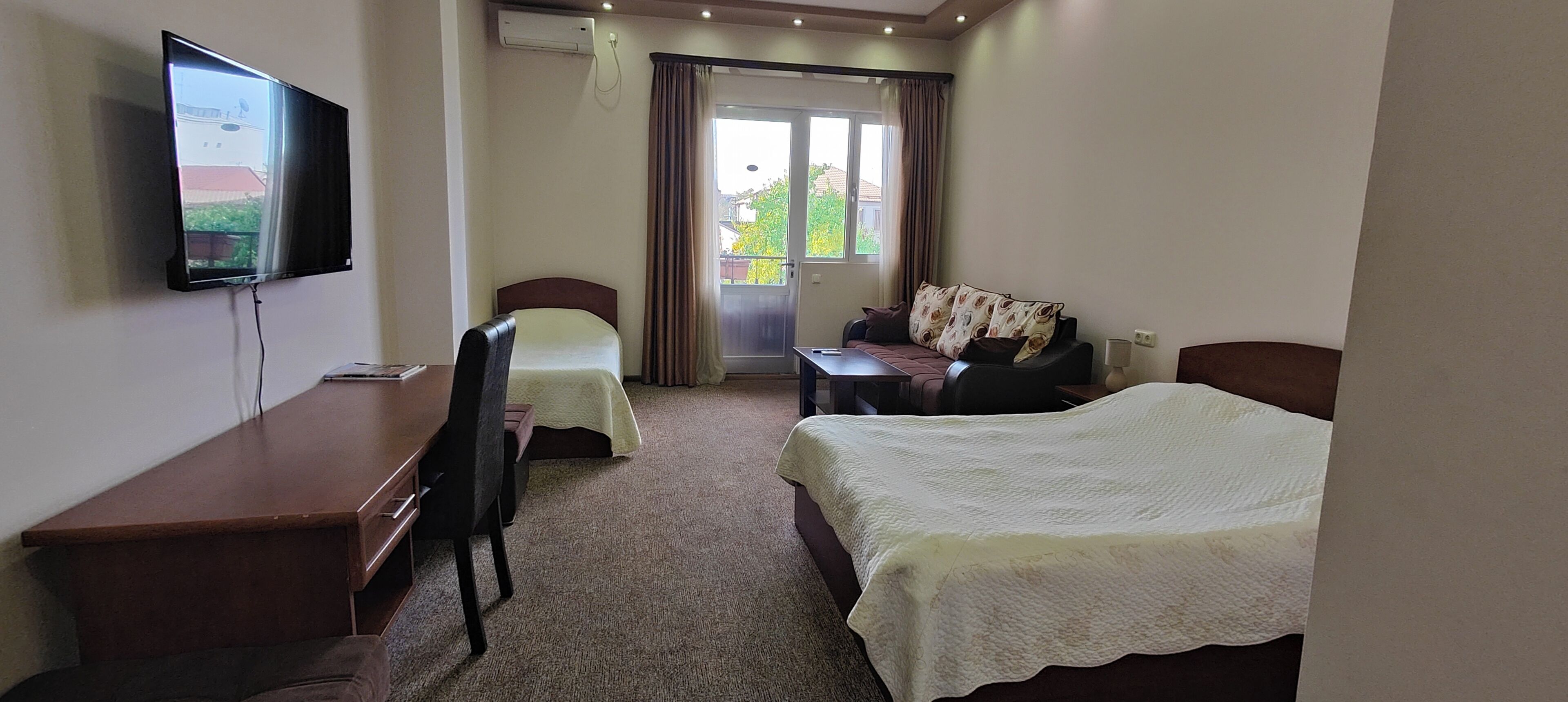 Ein Hotelzimmer mit Bett, Schreibtisch, Stuhl, Fernseher und Blick ins Freie.