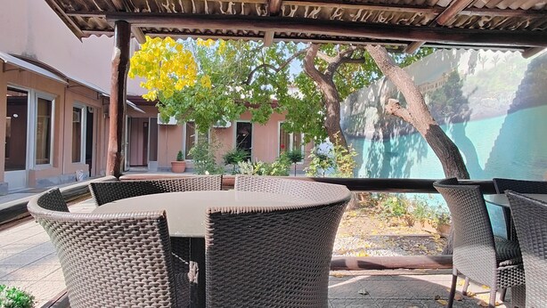 Ein überdachter Außenbereich mit Korbmöbeln, Blick auf einen Pool und einem Gebäude im Hintergrund.