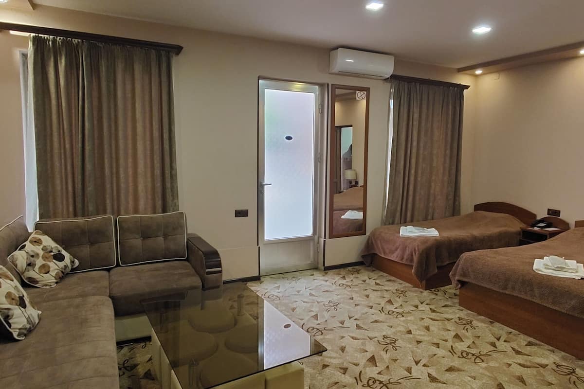 A hotel room with a sofa, two single beds, a glass coffee table, and a patterned carpet.