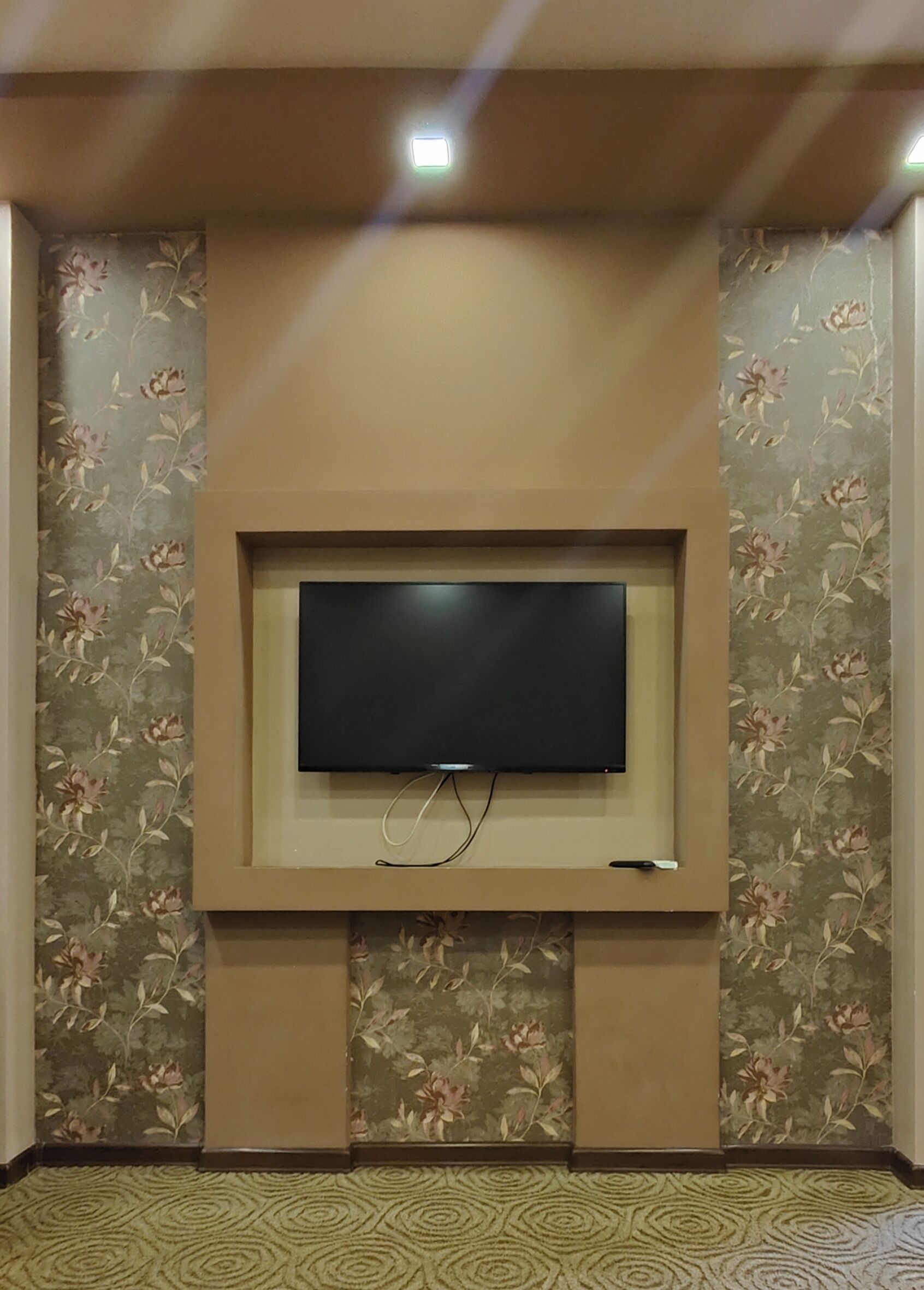 A flat-screen TV mounted on a wall with floral wallpaper.