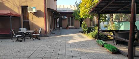 A covered outdoor seating area with tables and chairs, a potted plant, and a view of a body of water.