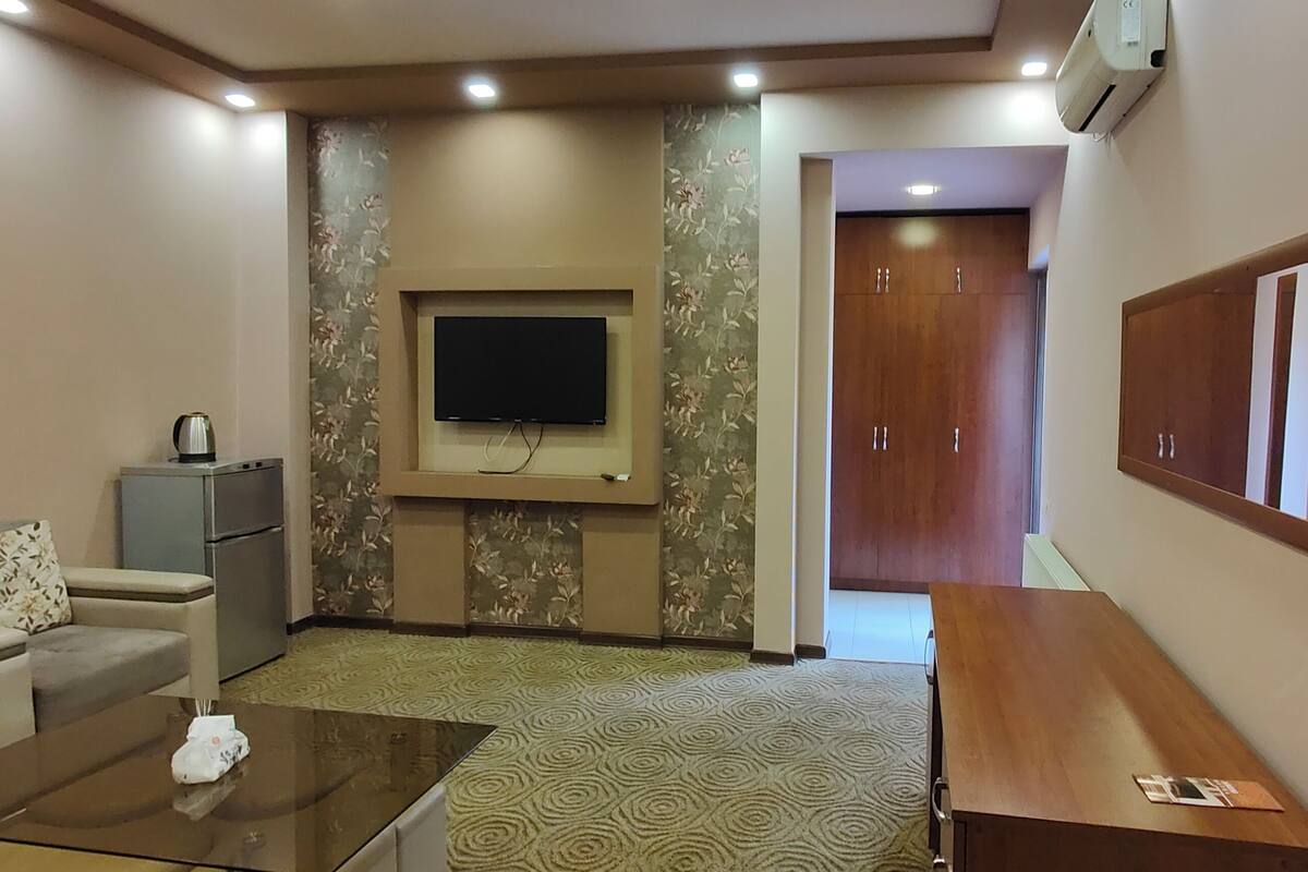 A modern living room with a sofa, a coffee table, a flat-screen TV mounted on the wall, and a wooden cabinet.
