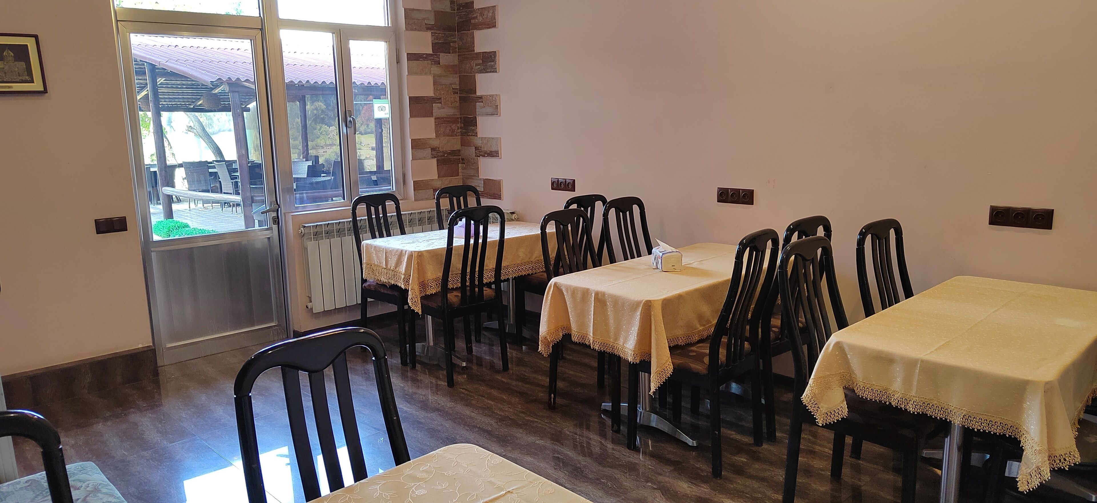 Un comedor con mesas y sillas, vista al exterior a través de una ventana, y una pared con diseño geométrico.