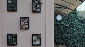 Ein Gebäude mit einer rosafarbenen Fassade, sechs gerahmten Blumendekorationen, einer Uhr und einer Treppe, die zu einem überdachten Bereich mit Topfpflanzen führt.