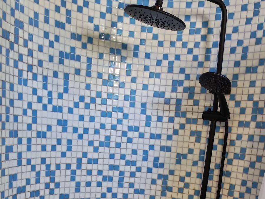 Ducha con manguera negra y cabezal de ducha manual, frente a una pared de azulejos con un diseño azul y blanco.