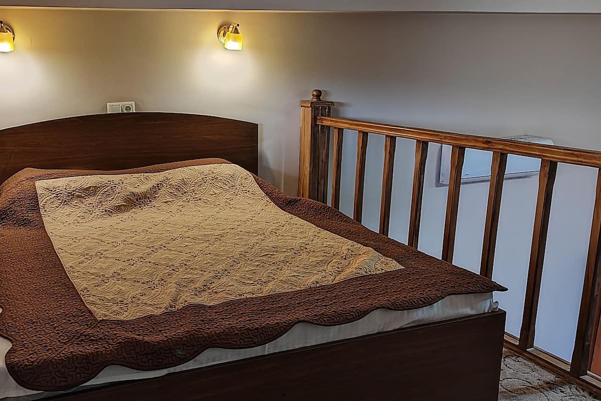 A bedroom with a wooden headboard, a patterned bedspread, and two wall-mounted lights.