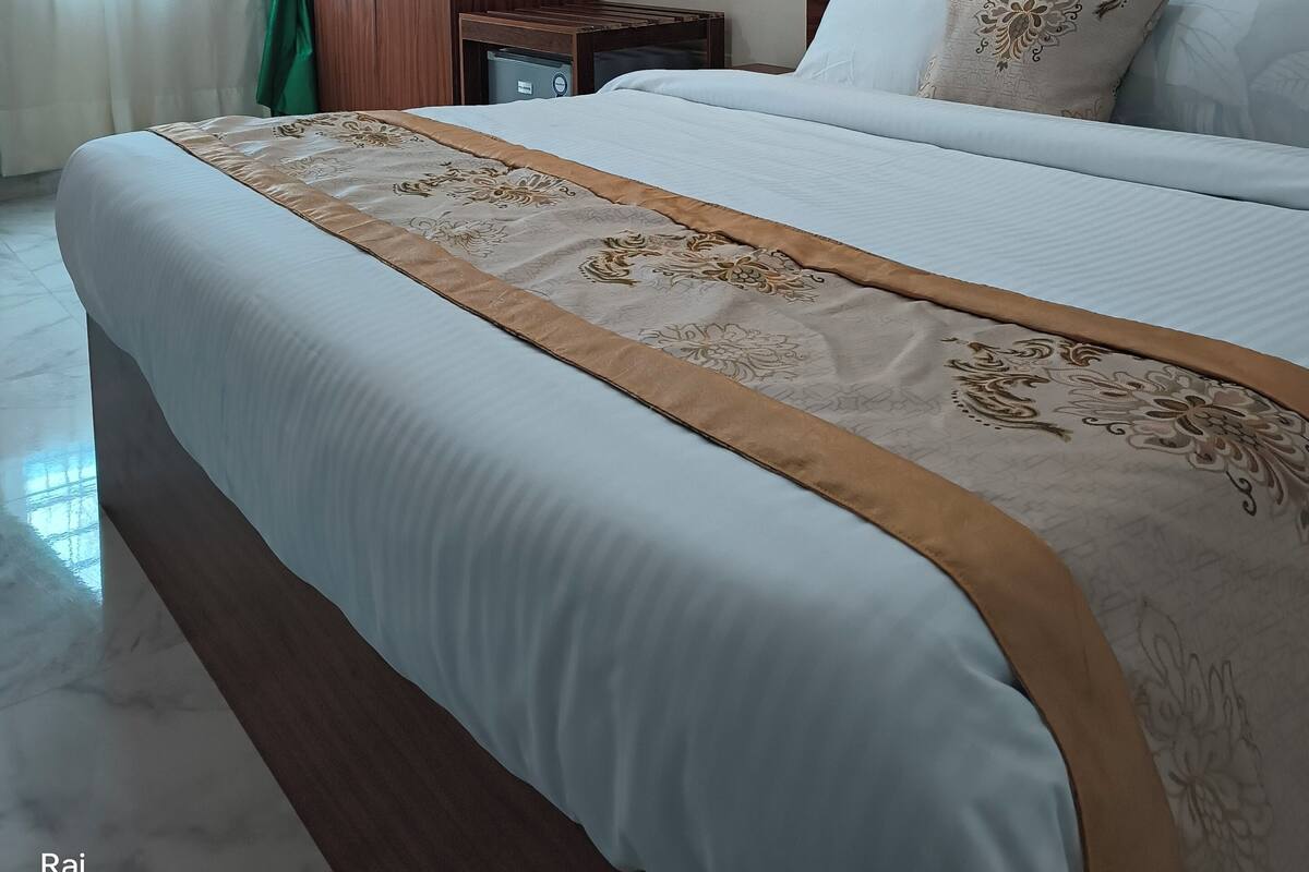 A hotel room with a large bed, a wooden wardrobe, a nightstand, and a wall-mounted air conditioner.