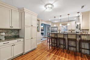 A kitchen with white cabinets, a wooden floor, and a central island with bar stools.