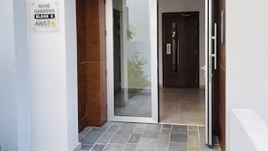 Una entrada moderna con puerta de vidrio, un camino empedrado de piedra y un letrero que indica 'ROSE GARDENS BLOCK C ARISTO DEVELOPERS'.