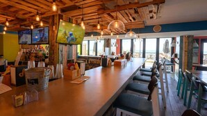 Um bar com vigas de madeira, luminárias pendentes e vista para o mar.
