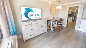 A modern kitchen with a dining area, a TV displaying 'BIG FISH Rentals', and a view into the adjacent room. - New Remodeled, Grand Cayman, Amazing Decor, Pools! (Myrtle Beach)