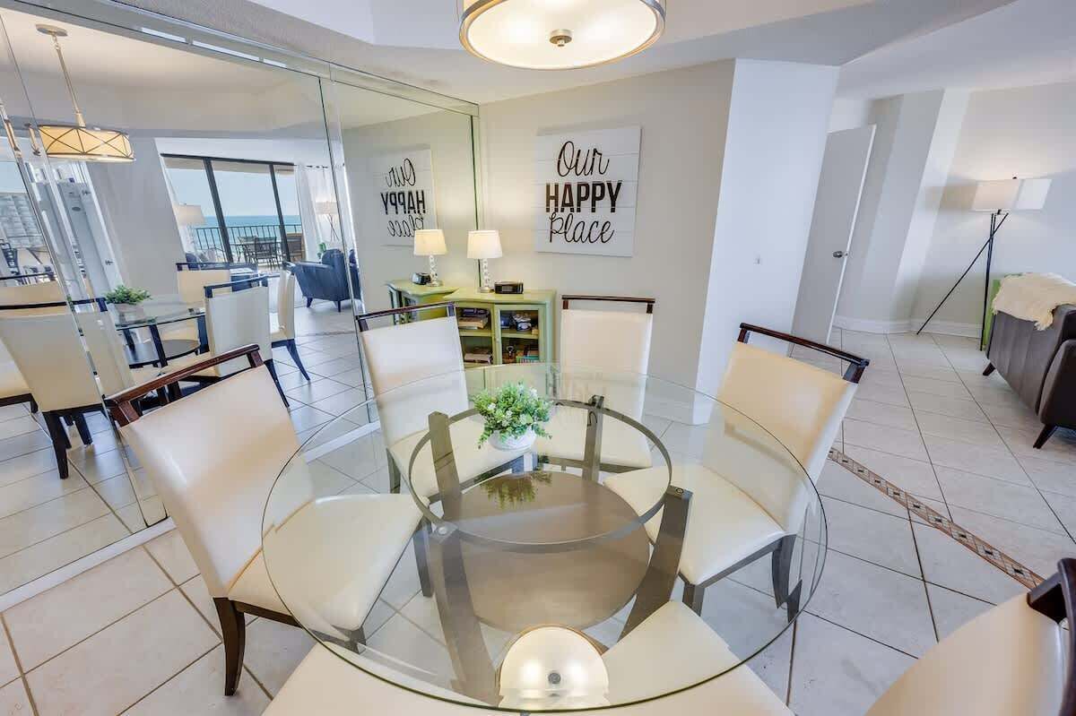 A modern dining area with a glass table and chairs, a small plant, and a wall with motivational text.